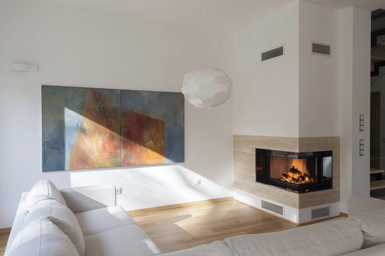Salon moderne avec canapé blanc d'angle face à une cheminée contemporaine à foyer vitré trois faces intégrée dans un habillage en pierre naturelle