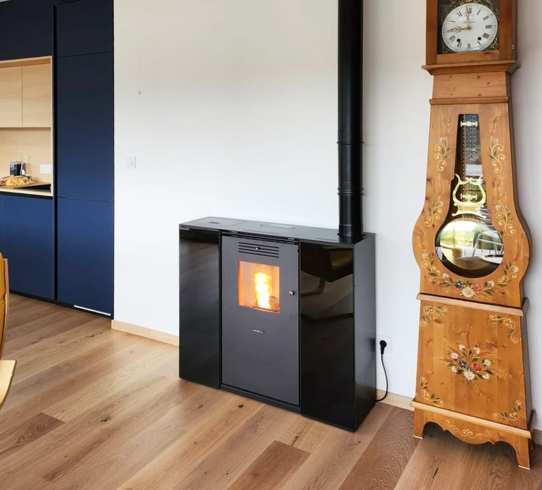 Intérieur moderne avec poêle à granulés noir laqué en fonte émaillée, vitre de combustion visible avec flamme active, conduit d'évacuation noir vertical