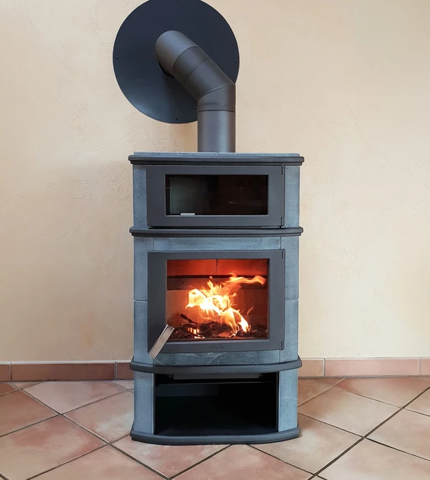 Poêle à bois design installé contre un mur intérieur crépis beige, sur carrelage terre cuite