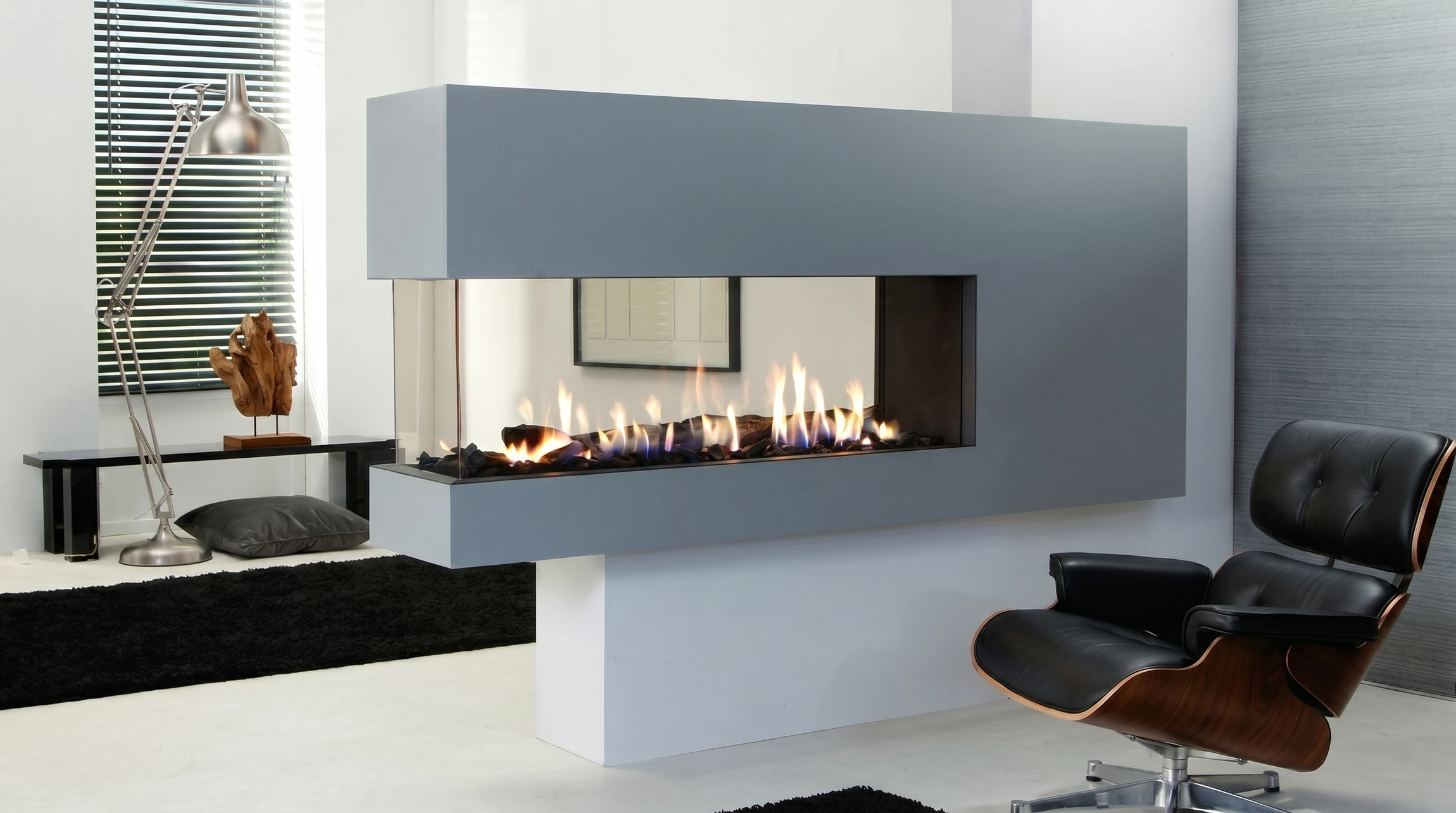 Cheminée moderne d'intérieur avec foyer linéaire à gaz, flammes bleues et jaunes s'élevant de roches volcaniques décoratives