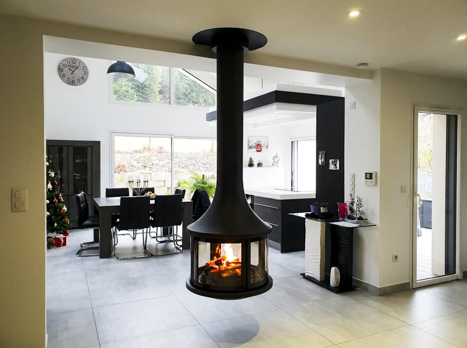 Salon moderne minimaliste avec cheminée double-face suspendue, encadrement en béton ciré gris, foyer linéaire panoramique vitré trois côtés, flammes gaz sur lit de galets noirs